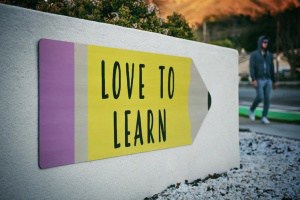 Il metodo per imparare l'inglese. Cartellone a forma di matita su un muro bianco: "love to learn", ragazzo che passa di lìper strada 